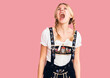 Young beautiful blonde woman wearing oktoberfest dress angry and mad screaming frustrated and furious, shouting with anger. rage and aggressive concept.