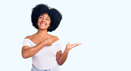 Sticker - Young african american girl wearing casual clothes amazed and smiling to the camera while presenting with hand and pointing with finger.