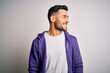 © Krakenimages.com - Young handsome man wearing purple sweatshirt standing over isolated white background looking away to side with smile on face, natural expression. Laughing confident.