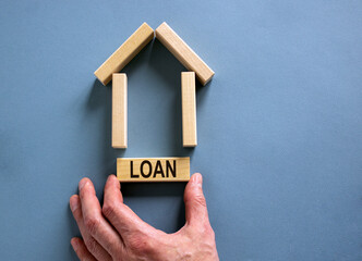 Male hand builds a model of a wooden house from wooden blocks. Word 'loan'. Copy space. Business concept. Beautiful blue background.