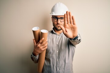 Wall Mural - Young architect man wearing contractor helmet holding project paper plan over isolated background with open hand doing stop sign with serious and confident expression, defense gesture