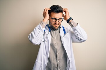 Sticker - Young doctor man wearing glasses, medical white robe and stethoscope over isolated background suffering from headache desperate and stressed because pain and migraine. Hands on head.