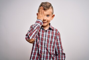 Wall Mural - Young little caucasian kid with blue eyes wearing elegant shirt standing over isolated background covering one eye with hand, confident smile on face and surprise emotion.