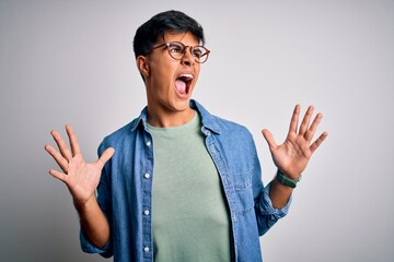 Poster - Young handsome man wearing casual shirt and glasses over isolated white background crazy and mad shouting and yelling with aggressive expression and arms raised. Frustration concept.