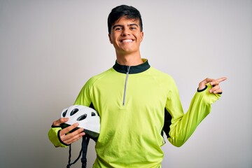 Poster - Young handsome cyclist man holding security bike helmet over isolated white background very happy pointing with hand and finger to the side