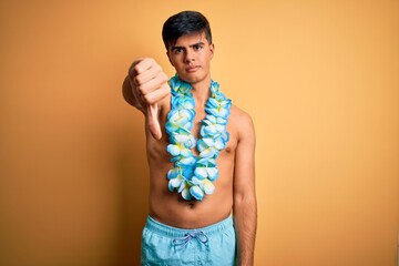 Poster - Young handsome tourist man on vacation wearing swimwear and hawaiian lei flowers looking unhappy and angry showing rejection and negative with thumbs down gesture. Bad expression.