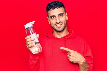 Wall Mural - Young hispanic man drinking bottle of water smiling happy pointing with hand and finger