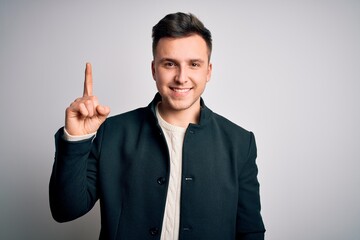 Wall Mural - Young handsome business mas wearing elegant winter coat standing over isolated background showing and pointing up with finger number one while smiling confident and happy.