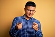 © Krakenimages.com - Young handsome latin man wearing casual shirt and glasses over yellow background pointing fingers to camera with happy and funny face. Good energy and vibes.