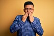 © Krakenimages.com - Young handsome latin man wearing casual shirt and glasses over yellow background laughing and embarrassed giggle covering mouth with hands, gossip and scandal concept