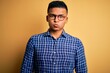 © Krakenimages.com - Young handsome latin man wearing casual shirt and glasses over yellow background puffing cheeks with funny face. Mouth inflated with air, crazy expression.