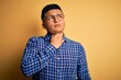 © Krakenimages.com - Young handsome latin man wearing casual shirt and glasses over yellow background Touching painful neck, sore throat for flu, clod and infection