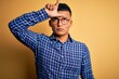 © Krakenimages.com - Young handsome latin man wearing casual shirt and glasses over yellow background making fun of people with fingers on forehead doing loser gesture mocking and insulting.