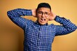 © Krakenimages.com - Young handsome latin man wearing casual shirt and glasses over yellow background Crazy and scared with hands on head, afraid and surprised of shock with open mouth