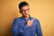 © Krakenimages.com - Young handsome latin man wearing casual shirt and glasses over yellow background Pointing with hand finger to the side showing advertisement, serious and calm face