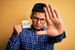 © Krakenimages.com - Young latin call center agent man overworked holding help message paper using headset with open hand doing stop sign with serious and confident expression, defense gesture