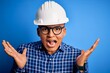 © Krakenimages.com - Young handsome engineer latin man wearing safety helmet over isolated blue background celebrating crazy and amazed for success with arms raised and open eyes screaming excited. Winner concept