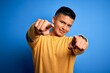 © Krakenimages.com - Young handsome latin man wearing yellow casual sweater over isolated blue background pointing to you and the camera with fingers, smiling positive and cheerful