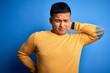 © Krakenimages.com - Young handsome latin man wearing yellow casual sweater over isolated blue background Suffering of neck ache injury, touching neck with hand, muscular pain