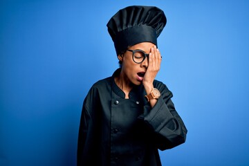 Wall Mural - Young african american chef woman wearing cooker uniform and hat over blue background Yawning tired covering half face, eye and mouth with hand. Face hurts in pain.