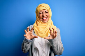 Sticker - Middle age brunette business woman wearing muslim traditional hijab over blue background smiling funny doing claw gesture as cat, aggressive and sexy expression