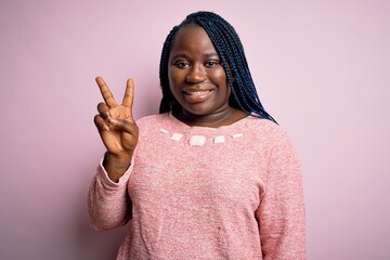 Sticker - African american plus size woman with braids wearing casual sweater over pink background showing and pointing up with fingers number two while smiling confident and happy.