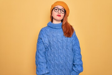 Poster - Young beautiful redhead woman wearing french beret and glasses over yellow background Relaxed with serious expression on face. Simple and natural looking at the camera.