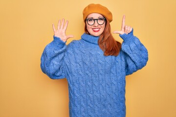 Wall Mural - Young beautiful redhead woman wearing french beret and glasses over yellow background showing and pointing up with fingers number seven while smiling confident and happy.