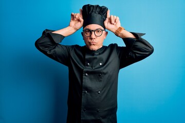 Sticker - Middle age handsome grey-haired chef man wearing cooker uniform and hat doing funny gesture with finger over head as bull horns