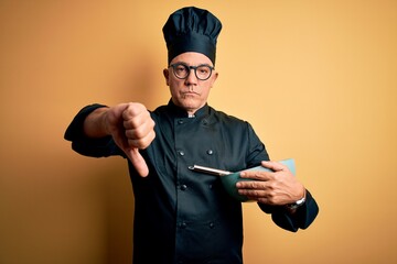 Wall Mural - Middle age handsome grey-haired chef man wearing cooker uniform and hat using whisk with angry face, negative sign showing dislike with thumbs down, rejection concept