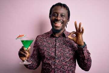 Poster - Young african american man drinking green cocktail. beverage over pink background doing ok sign with fingers, excellent symbol