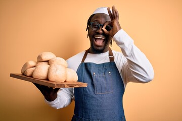 Sticker - Young african american baker man wearing apron holding tray with homemade bread with happy face smiling doing ok sign with hand on eye looking through fingers