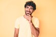 © Krakenimages.com - Handsome young man with curly hair and bear wearing casual tshirt over yellow background smiling looking confident at the camera with crossed arms and hand on chin. thinking positive.
