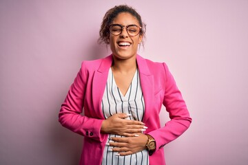 Wall Mural - Beautiful african american businesswoman wearing jacket and glasses over pink background smiling and laughing hard out loud because funny crazy joke with hands on body.