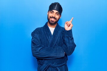 Poster - Young hispanic man wearing sleep mask and robe smiling happy pointing with hand and finger to the side