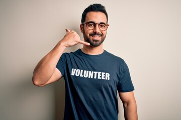 Handsome man with beard wearing t-shirt with volunteer message over white background smiling doing phone gesture with hand and fingers like talking on the telephone. Communicating concepts.