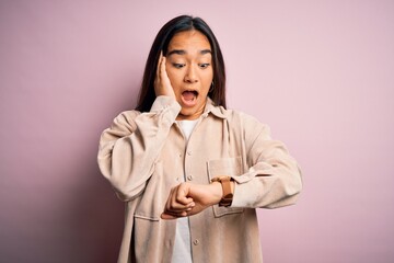 Sticker - Young beautiful asian woman wearing casual shirt standing over pink background Looking at the watch time worried, afraid of getting late