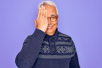 Poster - Middle age senior grey-haired man wearing glasses and winter sweater over purple background covering one eye with hand, confident smile on face and surprise emotion.