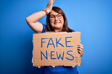 Beautiful plus size woman holding fake news banner for false journalism over isolated background stressed with hand on head, shocked with shame and surprise face, angry and frustrated. Fear and upset