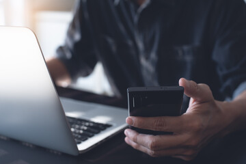 Wall Mural - Close up of man using mobile smartphone and working on laptop computer