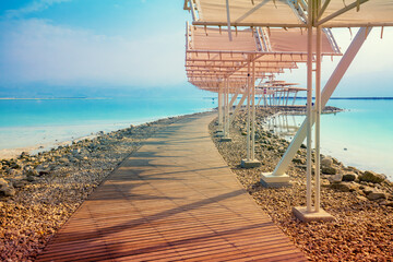 Fototapete - Seascape. The shore of the Dead Sea. Beach with a wooden walkway and sunshades. Summer. Israel