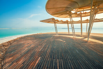 Fototapete - Seascape. The shore of the Dead Sea. Beach with a wooden walkway and sunshades. Summer. Israel