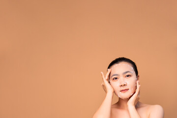 Portrait of Asian woman with facial mask standing isolated on beige background.