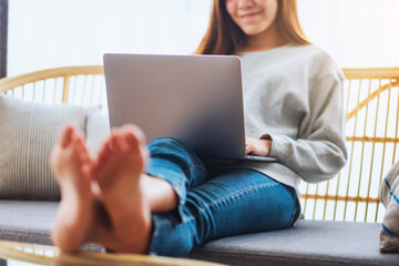 A beautiful woman using and working on laptop computer while lying on a sofa at home