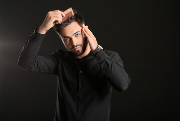 Wall Mural - Handsome man combing hair on dark background