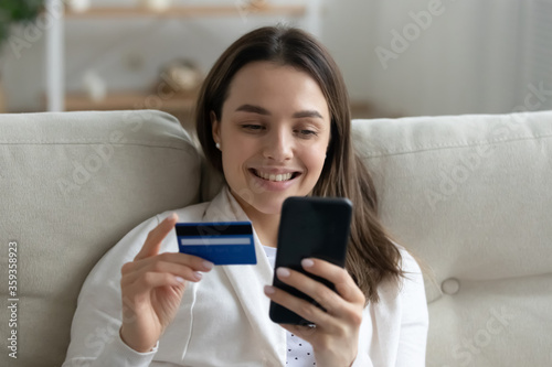 Fotografía Woman shopper sit on sofa spend money via e-commerce e-stores, enjoy purchase in internet using easy method, paying hold credit card and smartphone