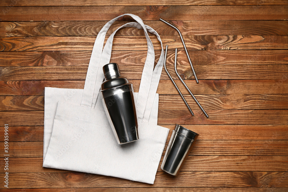 Eco bag with shaker and cocktail straws on wooden background