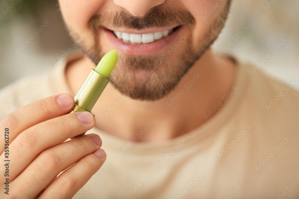 Handsome young man with lip balm at home, closeup