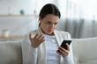 © fizkes - Irritated woman sit on couch holding smart phone feels annoyed network wi-fi connection lost, slow device, received unpleasant message bad sms, having problems with gadget, need repair service concept