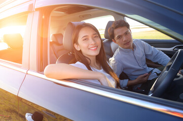 Young couple in his car, happy to drive on a country road. Happy young women and young men in car